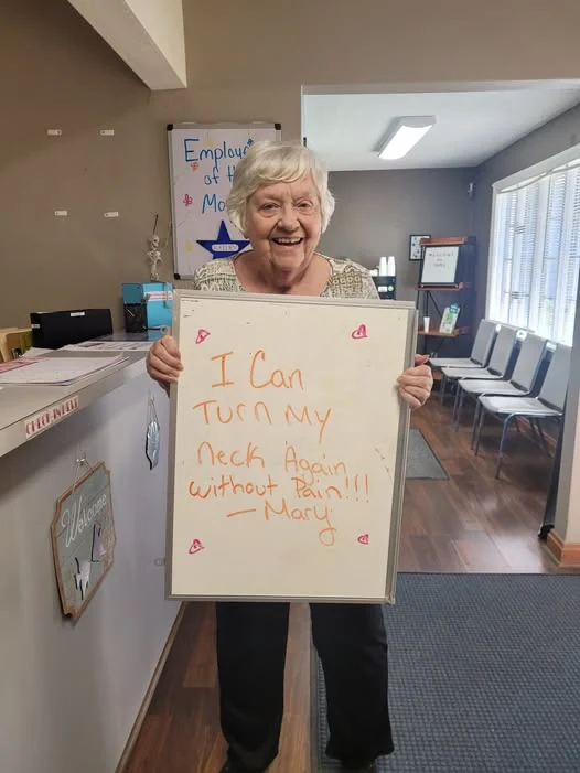 Mary, a patient at Greenville Rehab and Pain Clinic, holding a sign reading I can turn my neck again without pain